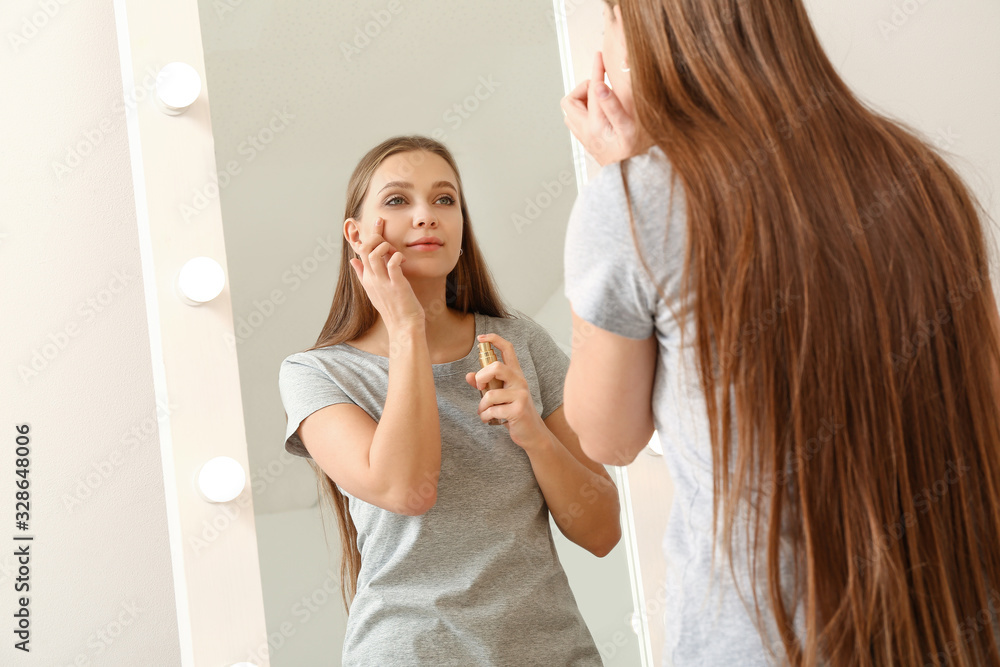 Beautiful young woman applying face serum in front of mirror at home