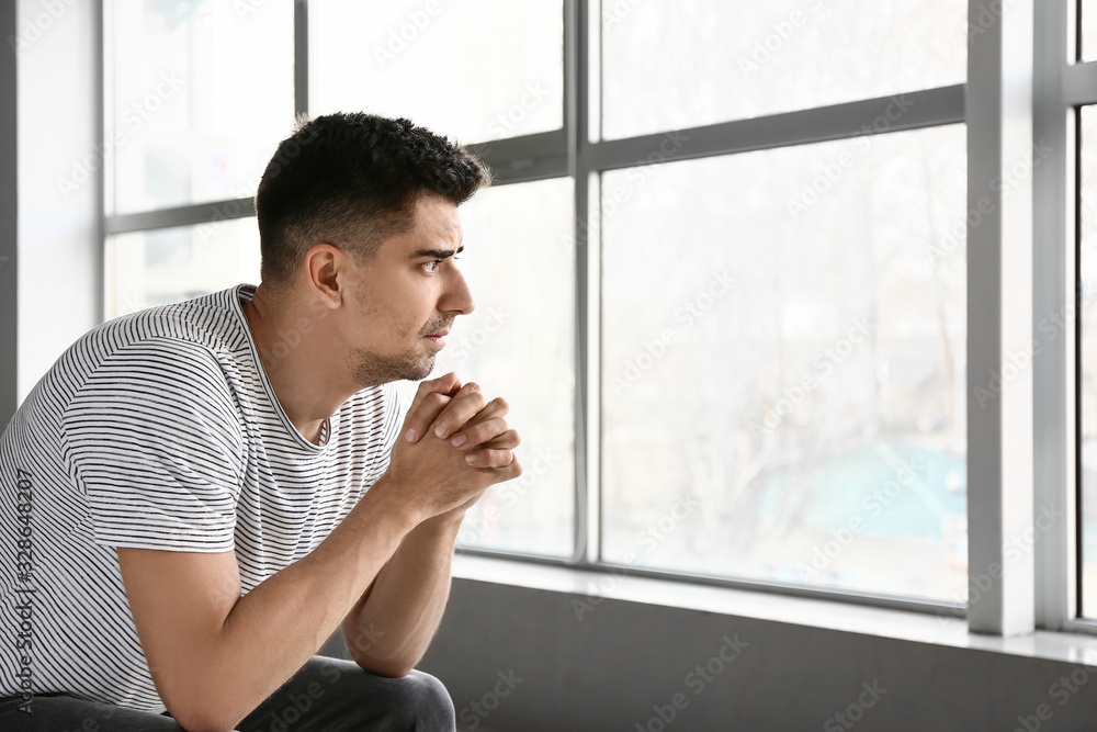 Depressed young man near window