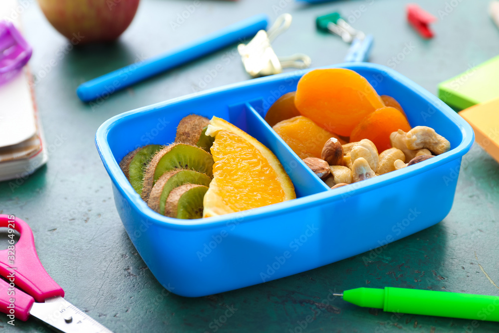 School lunch box with tasty food and stationery on table