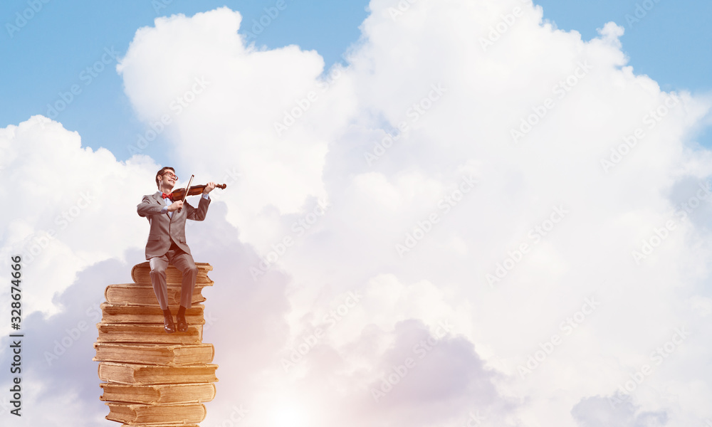 Handsome violinist in blue day sky on pile of books play his melody