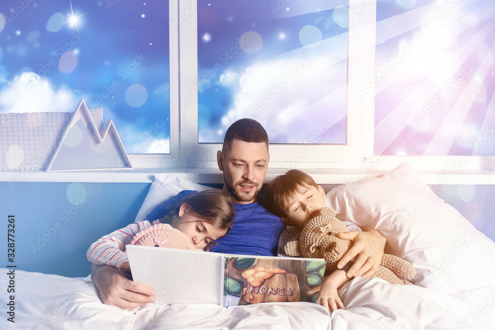 Father reading bedtime story to his little children at home