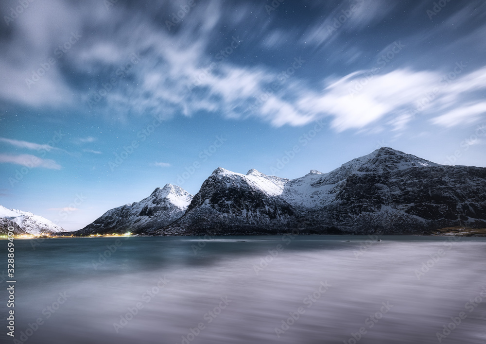 Mountains and reflections on water at night. Winter landscape. The sky with stars and clouds in moti