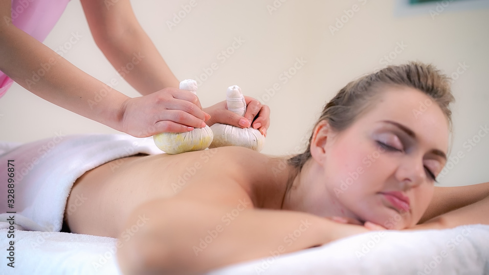 Massage therapist holds a herbal compress to do treatment to woman lying on spa bed in a luxury spa 