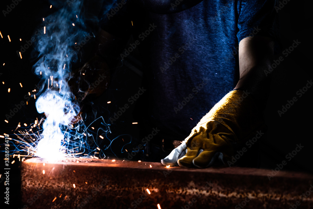 Metal welder working with arc welding machine to weld steel at factory while wearing safety equipmen