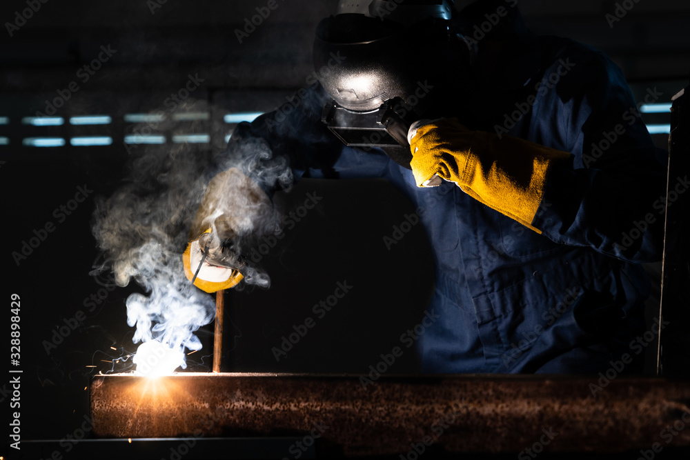 Metal welder working with arc welding machine to weld steel at factory while wearing safety equipmen