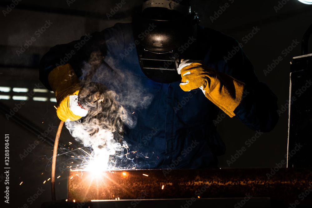 Metal welder working with arc welding machine to weld steel at factory while wearing safety equipmen