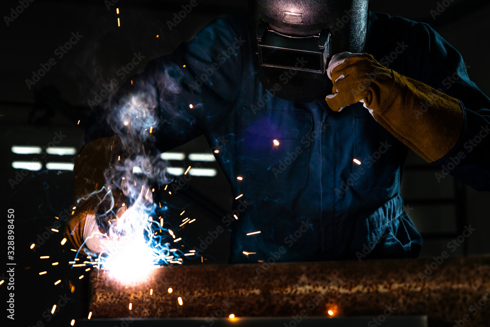 Metal welder working with arc welding machine to weld steel at factory while wearing safety equipmen