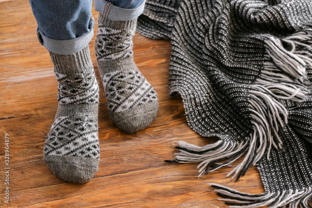 Legs of woman in knitted socks and plaid on wooden background