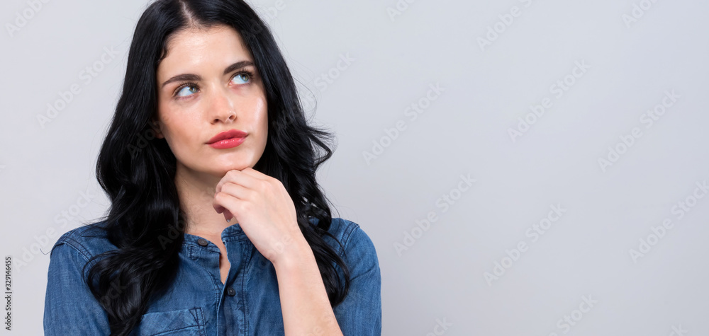 Young woman in a thoughtful pose on a gray background