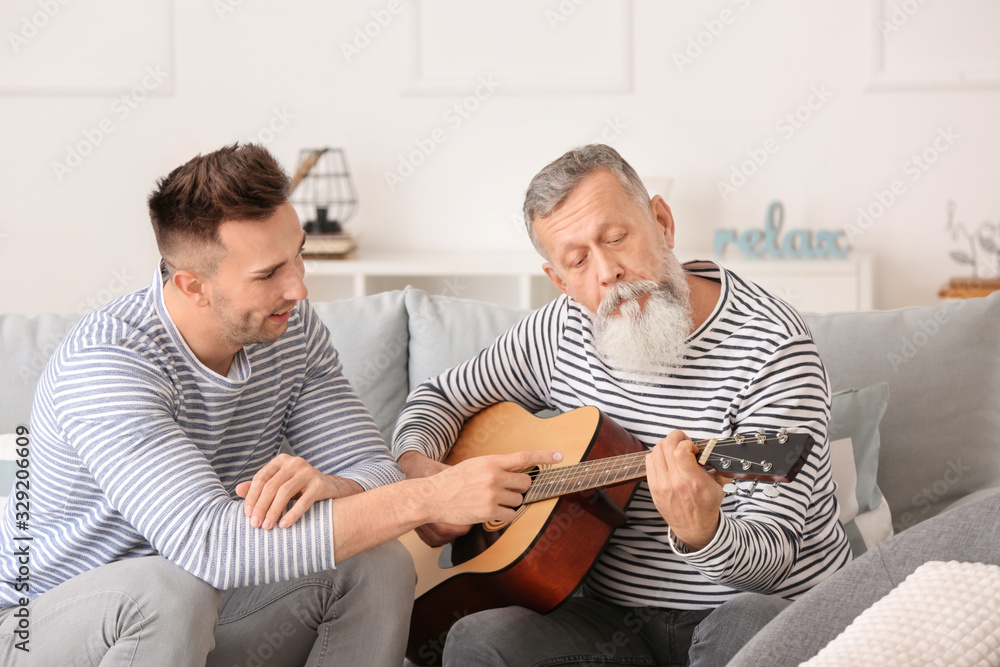 Young man with his father playing guitar at home