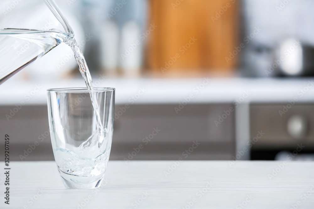 Pouring of fresh water into glass on table in kitchen