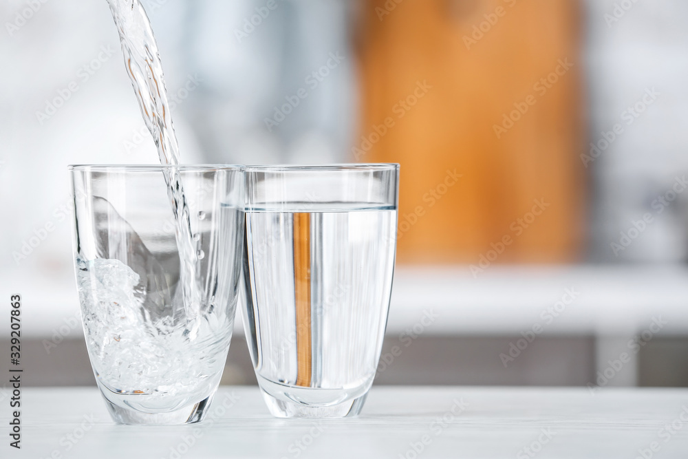 Pouring of fresh water into glass on table in kitchen