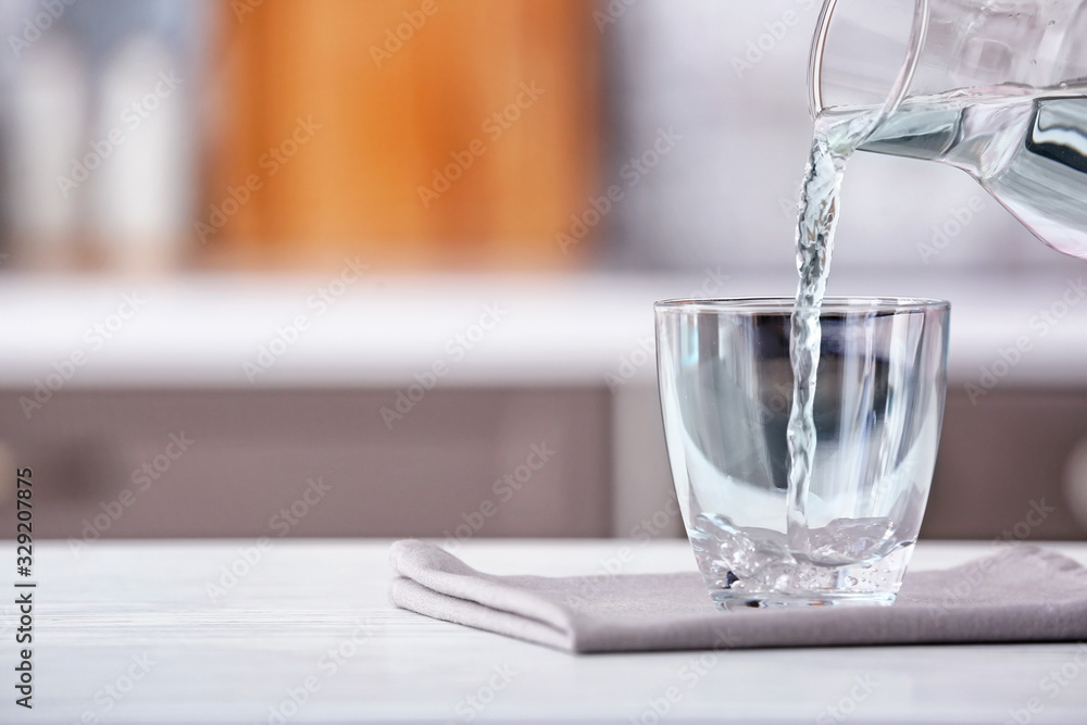 Pouring of fresh water into glass on table in kitchen