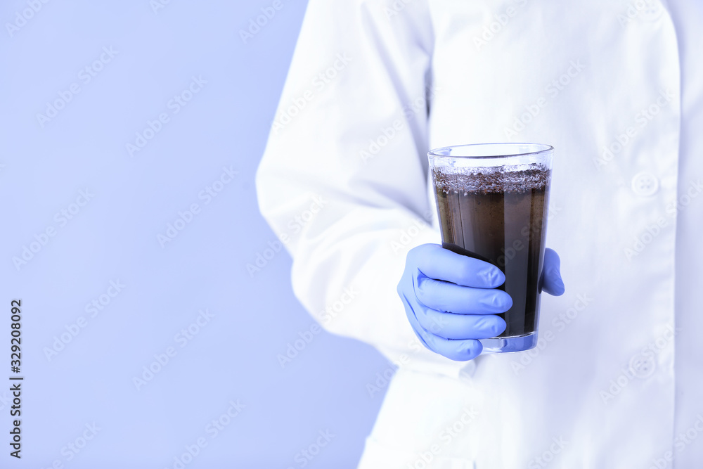 Female doctor with glass of dirty water on color background, closeup