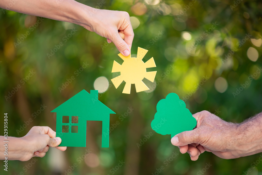 Family holding house in hands against spring green background