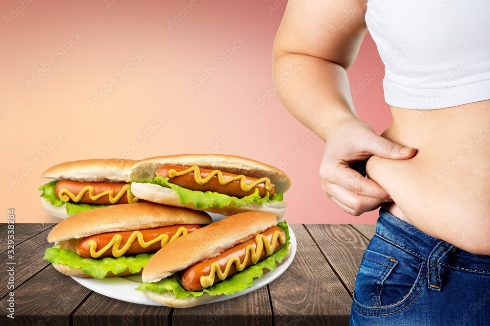 Womans hand holding excessive belly fat and hot dogs