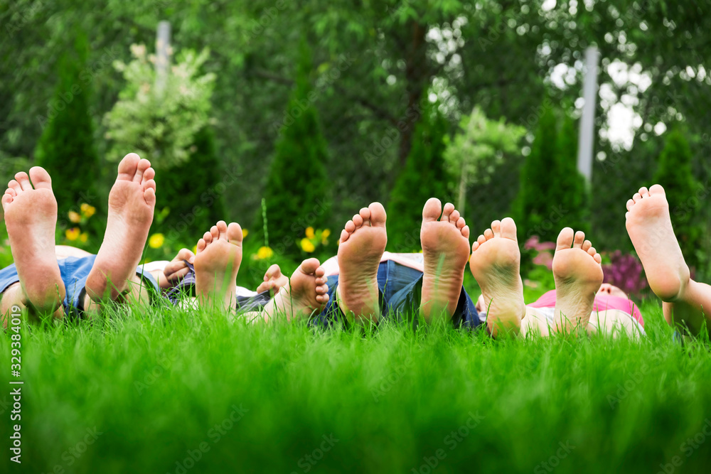 Family relaxing on green grass, barefoot laying down and looking into the sky