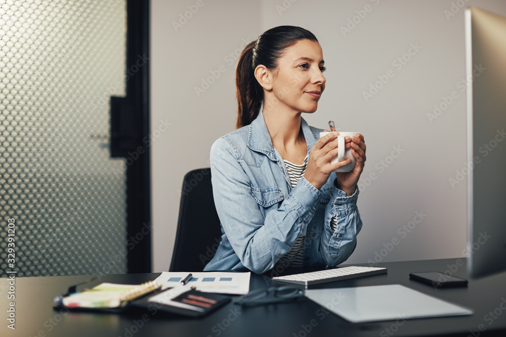 Smiling businesswoman drinking tea while working at her desk