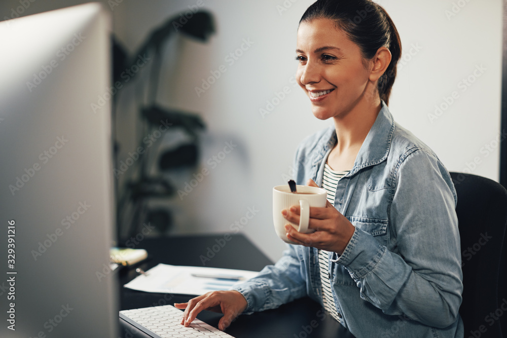 Smiling businesswoman working at her desk and drinking tea