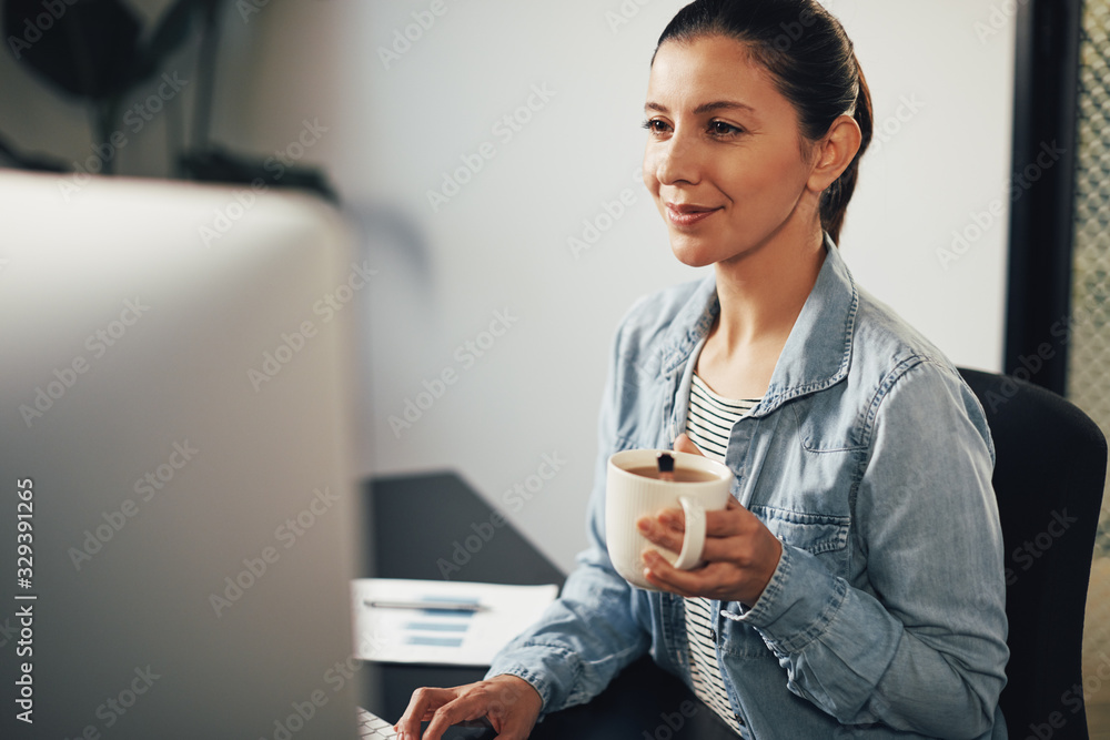 Smiling businesswoman drinking tea and working on a computer