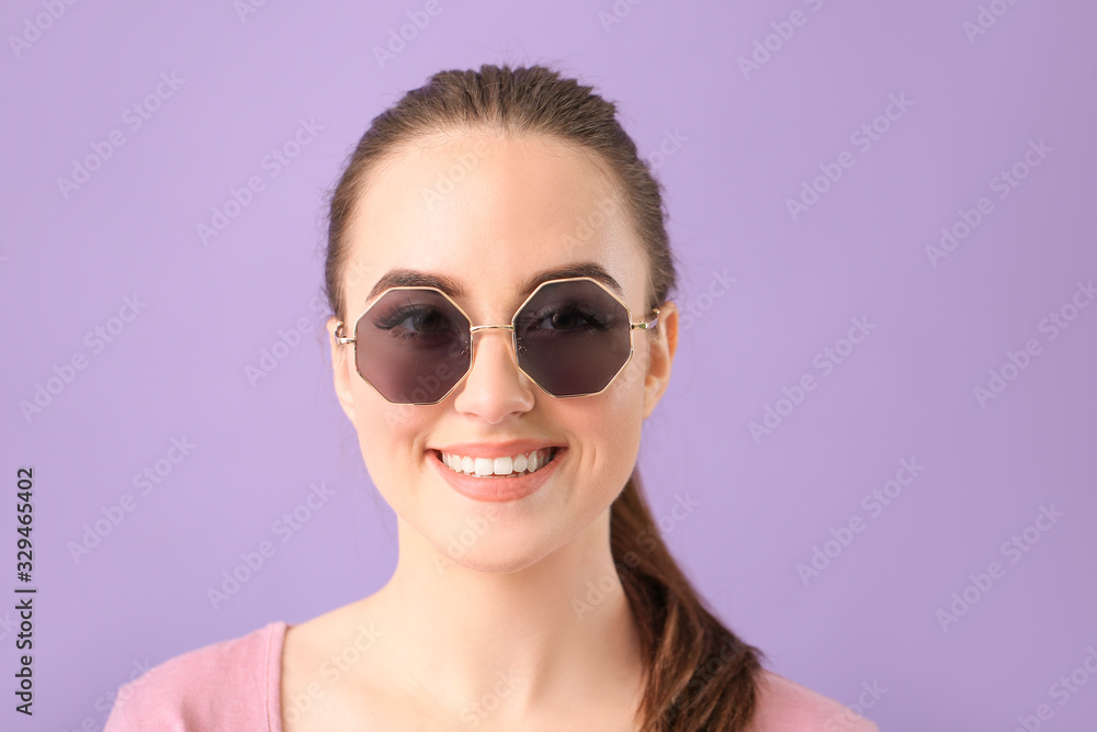 Young woman with stylish sunglasses on color background