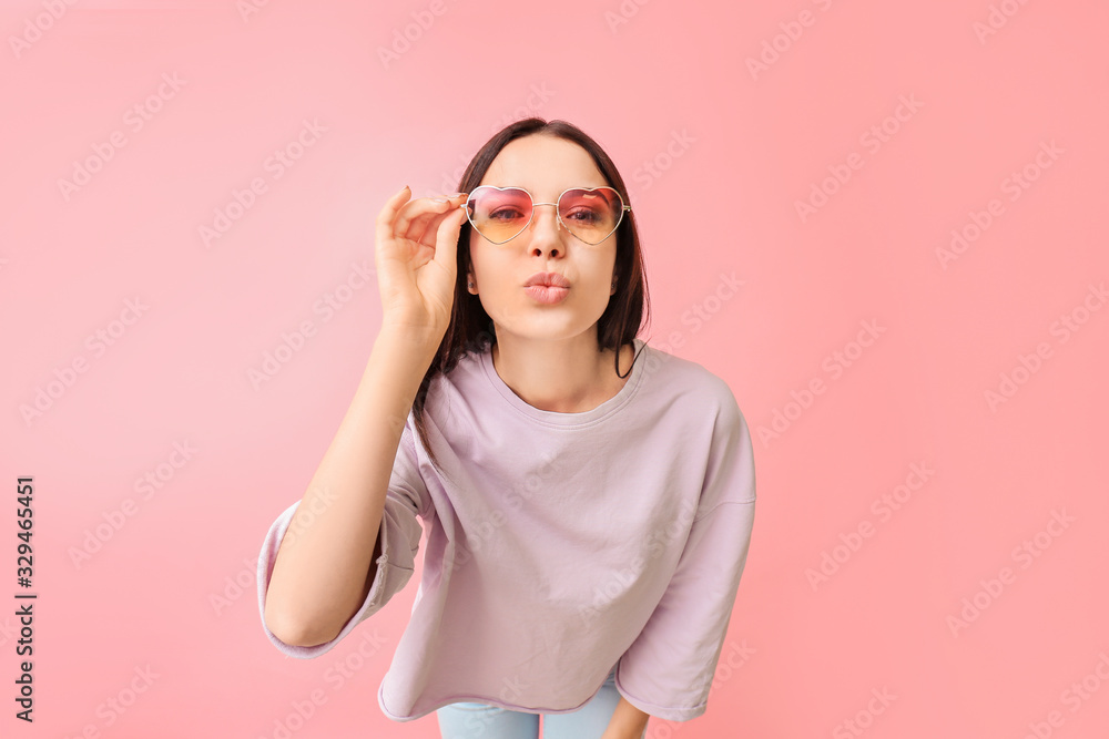 Young woman with stylish sunglasses on color background