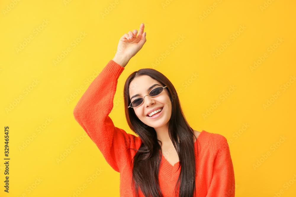 Young woman with stylish sunglasses on color background