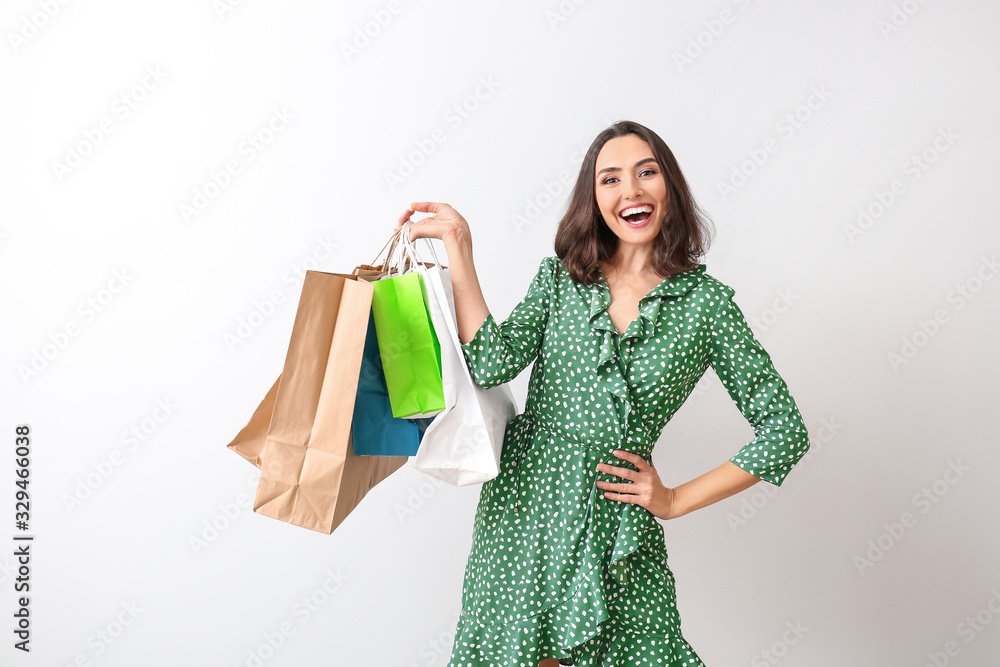 Beautiful young woman with shopping bags on light background