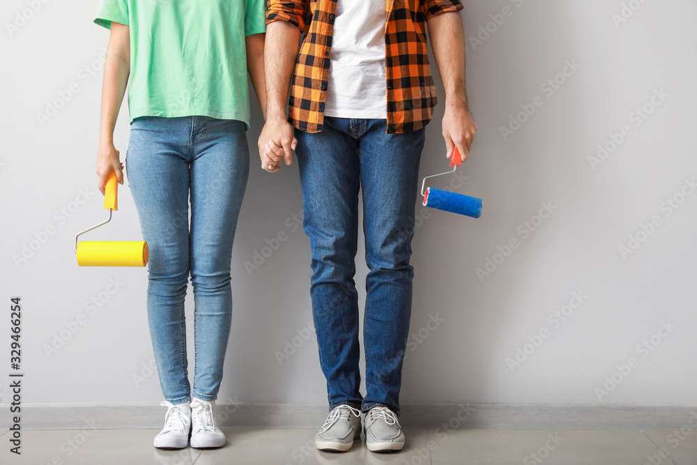 Young couple with paint rollers near light wall in new apartment