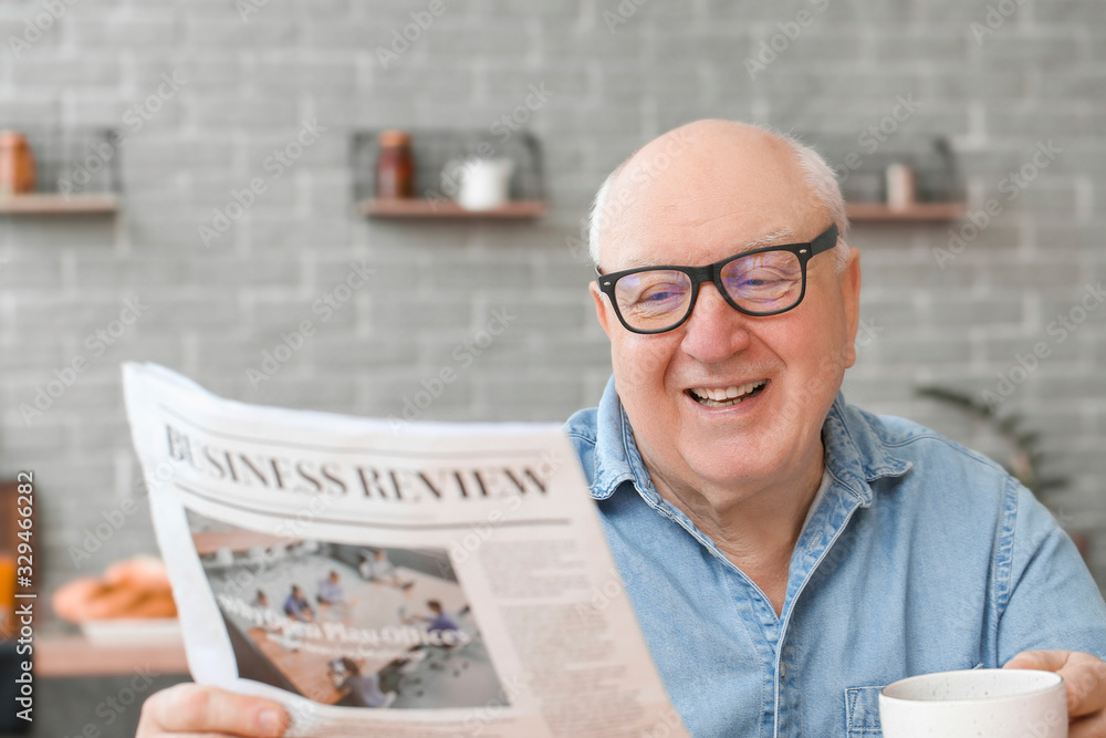 Portrait of elderly man drinking tea while reading newspaper at home