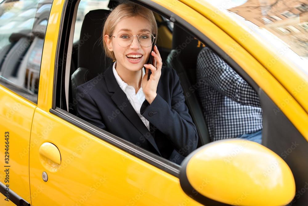 Young businesswoman talking by phone while sitting in taxi