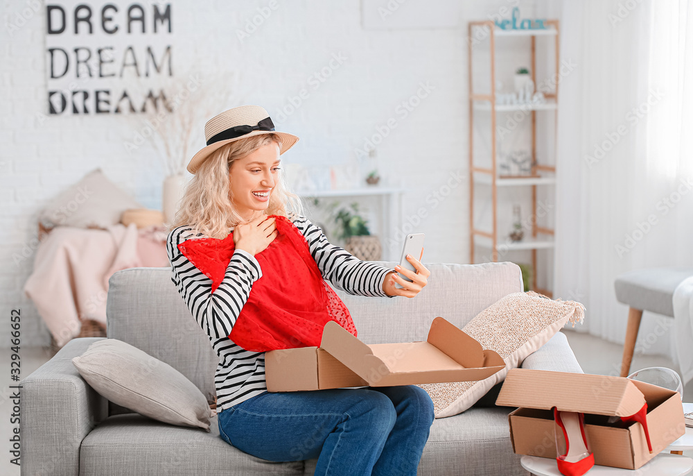 Happy young woman unpacking box with new clothes at home