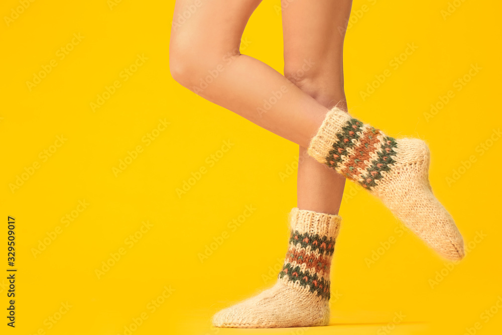 Legs of young woman in warm knitted socks on color background