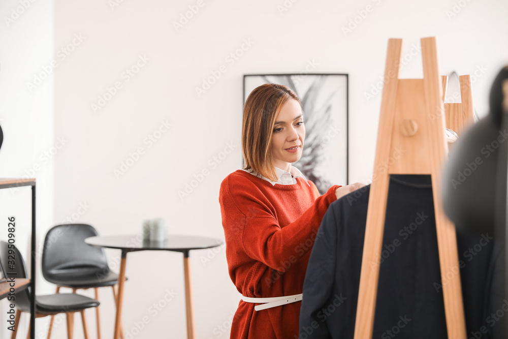 Female stylist near rack with male clothes in her studio