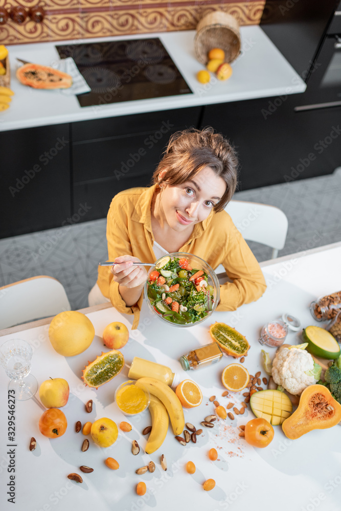 一个年轻快乐的女人在餐桌上吃沙拉的画像，餐桌上摆满了健康的生蔬菜和油炸食品