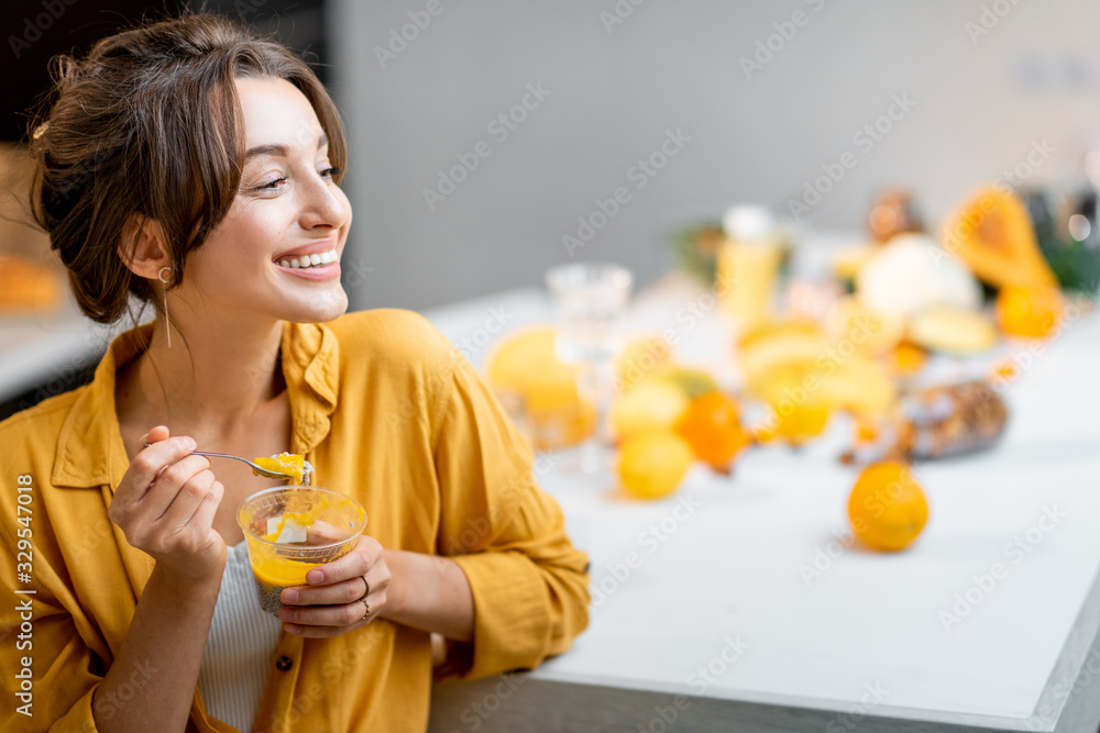 Portrait of a young and cheerful woman eating chia pudding, having a snack or breakfast in the kitch