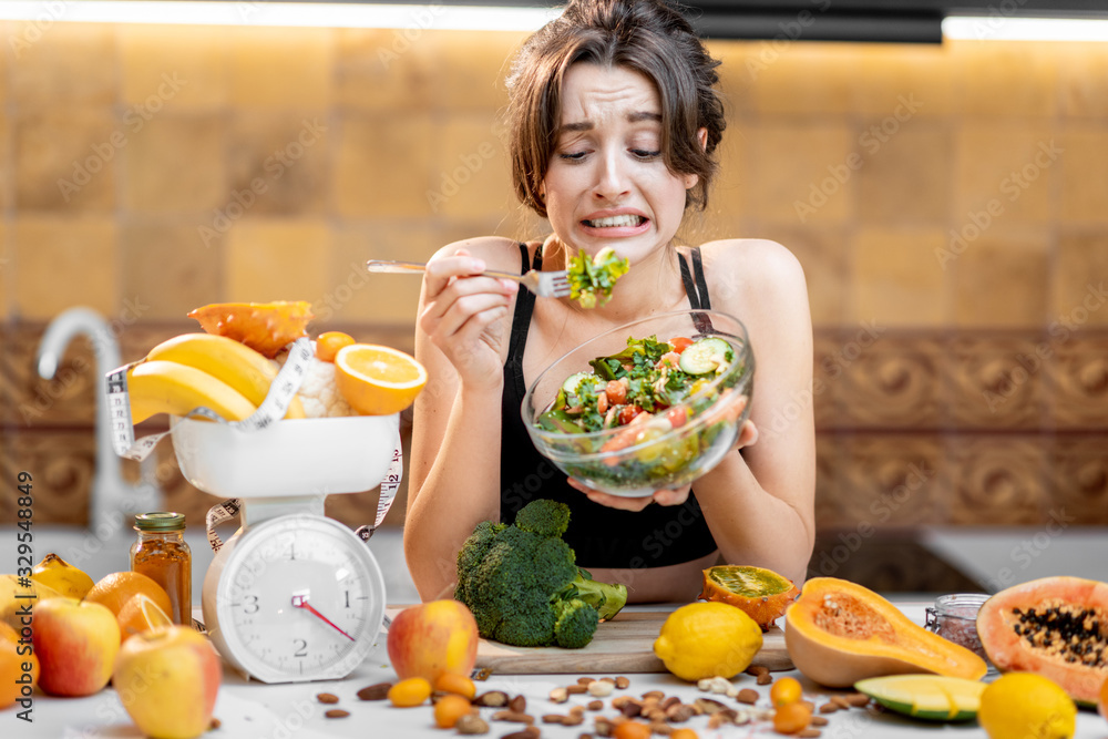 运动女性吃沙拉，厨房里有很多健康的新鲜食物。losin的概念