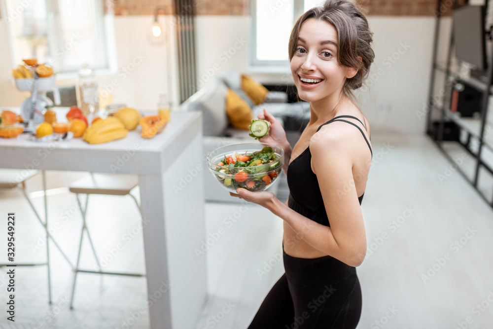 Portrait of a cheerful athletic woman eating healthy salad during a break at home. Concept of losing