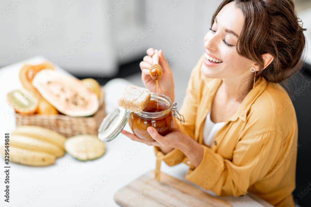 Portrait of a young and cheerful woman with a jar full of sweet honey on the kitchen at home