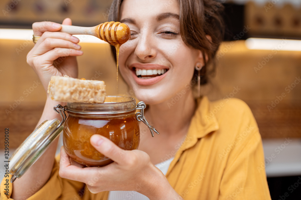 Portrait of a young and cheerful woman with a jar full of sweet honey on the kitchen at home