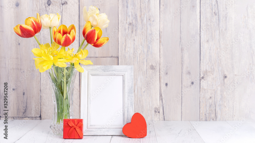 Tulip flower in glass vase with picture frame decor on wooden table background wall at home, close u