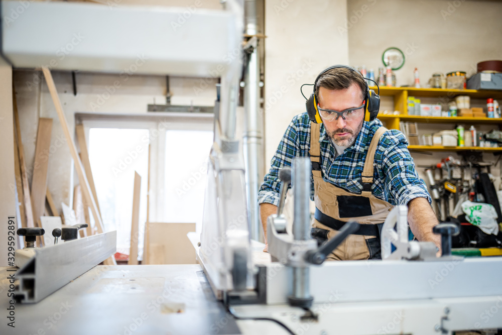 Carpenter using circular saw to cut a large wooden board at carpentry workshop