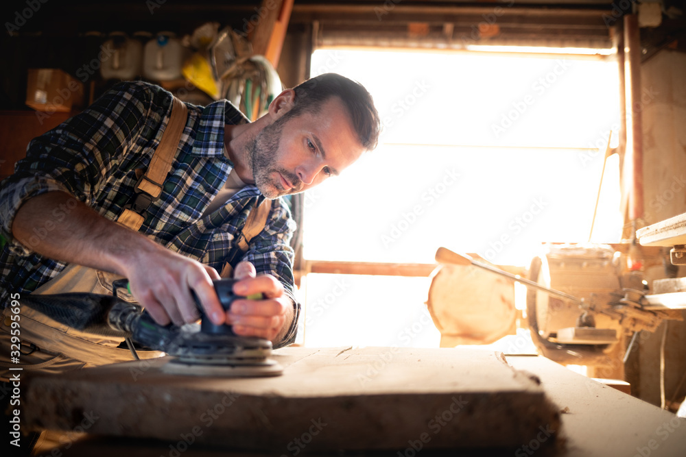 Carpenter at workshop polishes wooden board with a electric orbital sander