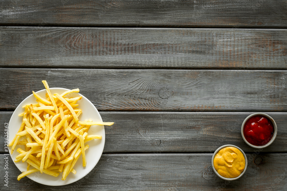 Potato chips on plate near sauces on dark wooden table top-down copy space