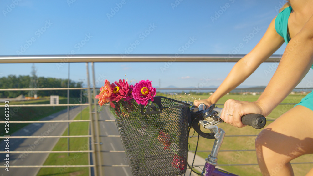 CLOSE UP: Unrecognizable woman rides her bicycle with a bouquet in the basket.