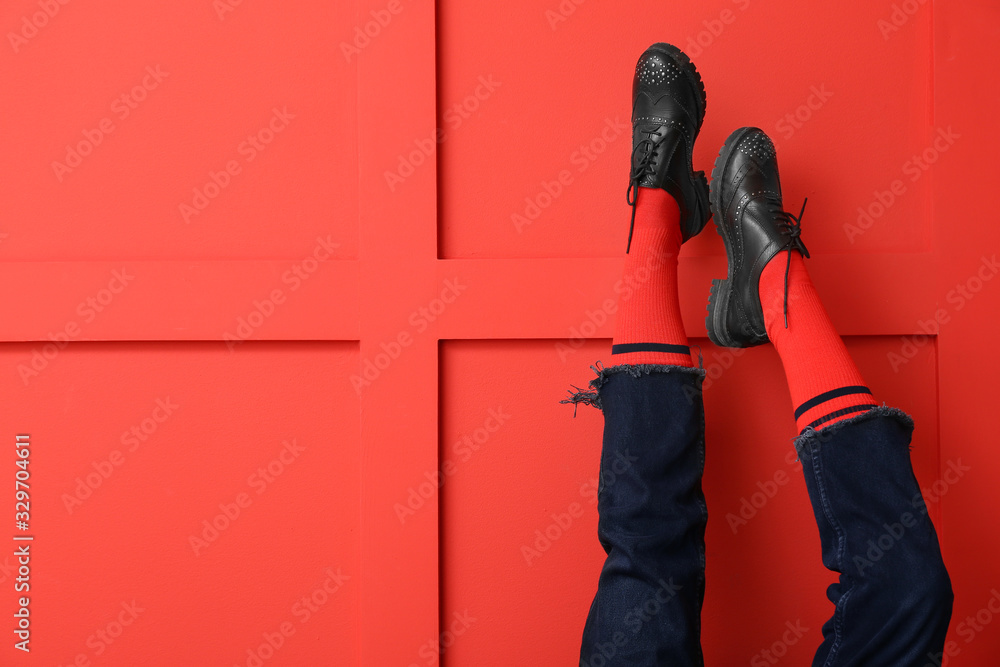 Legs of young woman in socks, shoes and jeans on color background