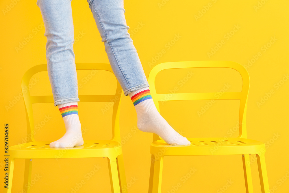 Legs of young woman in socks standing on chairs against color background