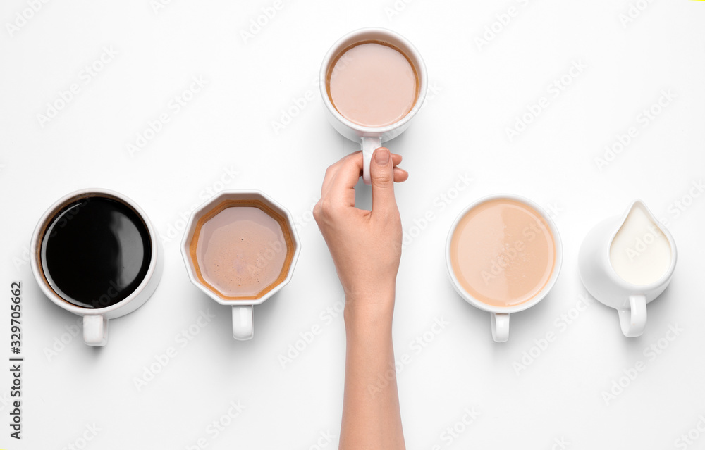 Female hand and cups of different coffee on white background