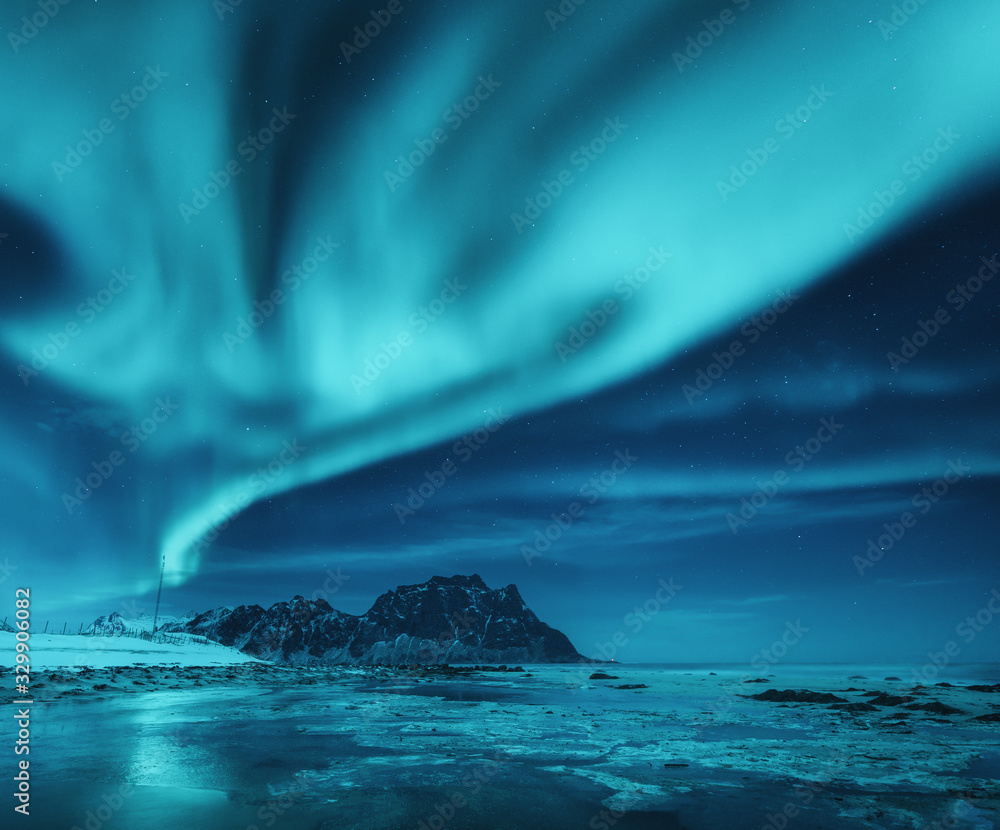 Northern lights over the snowy mountains and sandy beach in winter. Aurora borealis in Lofoten islan