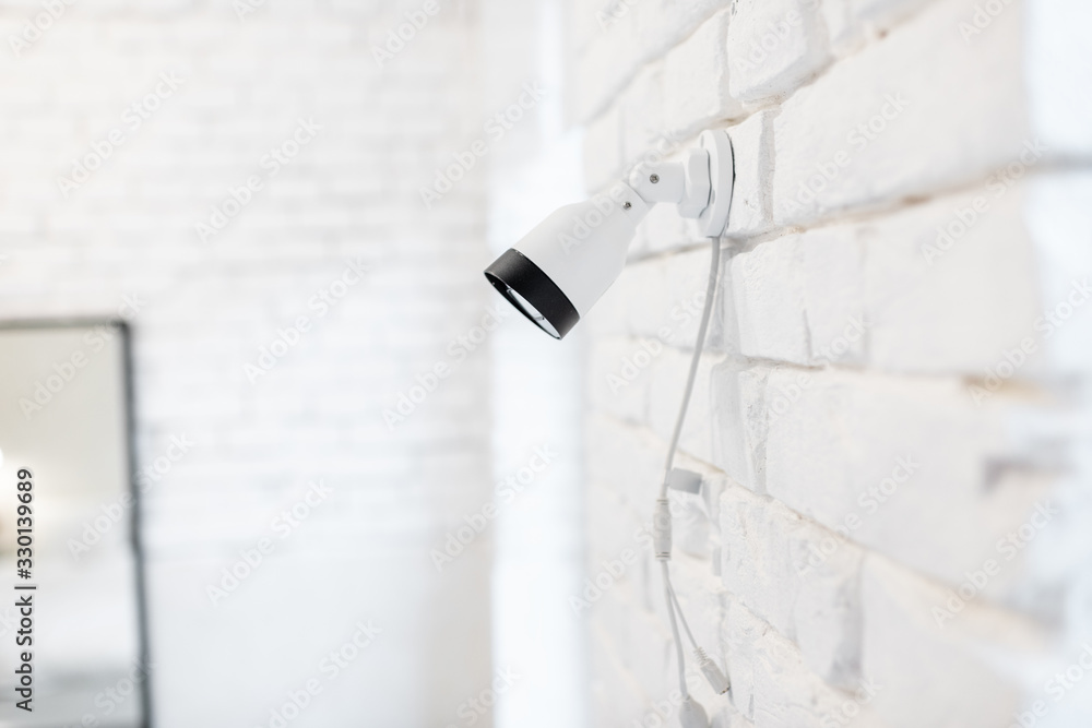 Surveillance ip camera mounted on the white brick wall indoors. Home video surveillance concept